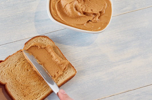 A knife with peanut butter being spread on toast.